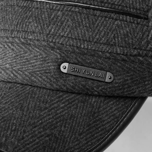 Detail of wool-like herringbone fabric with branded metal plate and leather edging