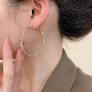 Close-up of model wearing large gold twisted hoop earrings with a textured metal finish