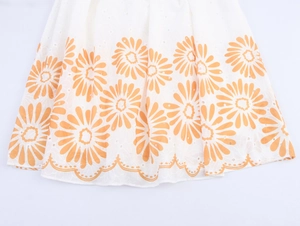 Détail de l'ourlet festonné avec broderie marguerite orange sur robe blanche ajourée