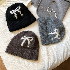 Detail of plush knit beanies with bow patterns in black, grey, and coffee colors