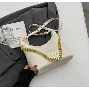 Detailed shot of white quilted shoulder bag with chunky gold chain on grey blazer