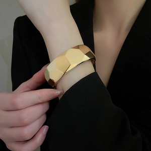 Detail shot of wide gold geometric bangle with faceted design on a model's wrist