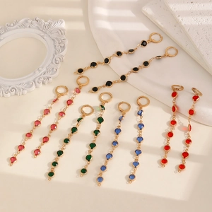 Boucles d'oreilles pendantes dorées avec pierres précieuses sur fond de pierre