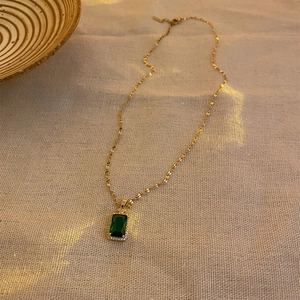 Vintage gold necklace with square emerald crystal pendant and diamonds on linen background