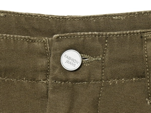 Detail of metal button with Fashion Jeans engraving and stitching on brown canvas pants