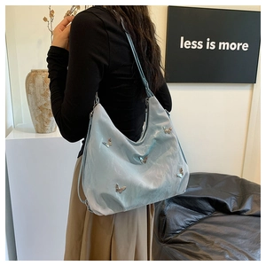 Detail of light blue tote bag with silver butterfly charms worn on shoulder in minimalist setting
