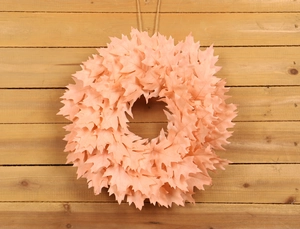 Pink decorative wreath with faux bodhi leaves on a light wood background for home decor