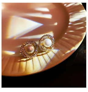 Macro shot of gold spiral earrings with sparkling rhinestones and center pearl on ceramic