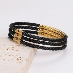 Detail of three-layer black steel cable bracelets with gold-plated metal accents
