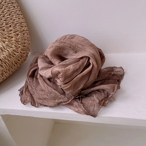 Detailed texture of brown pleated silk scarf paired with a woven straw bag for causal style