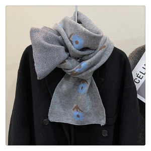 Detailed knit texture of a grey scarf with blue flower patterns on a black coat
