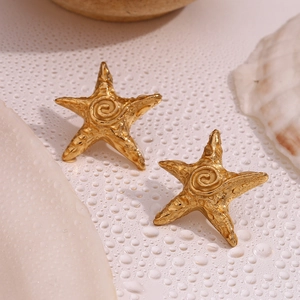 Macro detail of gold starfish stud earrings with spiral texture on shell background