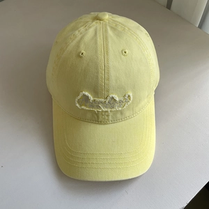 Close-up of yellow cotton baseball cap featuring embroidered patch with frayed edges
