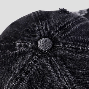 Detailed close-up of stitching and button on washed black denim baseball cap