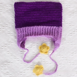 Detail of purple knitted baby hat with ear flaps and yellow crochet star tassels