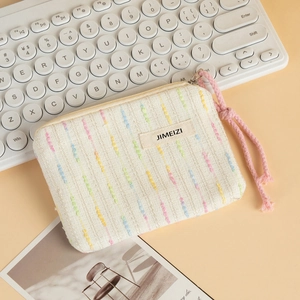 Detail of white textured fabric makeup bag with rainbow stripes and a pink rope handle