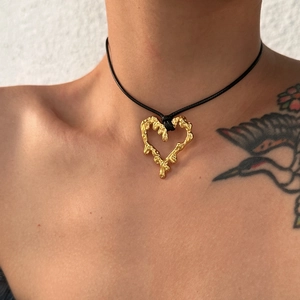 Detailed view of a gold lava-textured heart pendant on a black cord necklace worn on neck