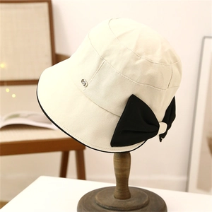Chic beige bucket hat with large brim, black ribbon bow, and stylish metal logo accent