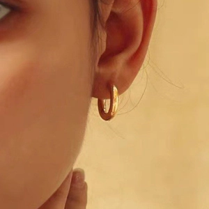 Close-up of classic gold-plated titanium steel hoop earrings worn on a female ear model
