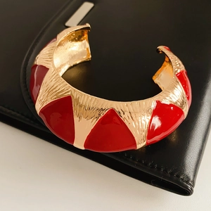Close-up of vintage wide open bangle with red enamel geometric patterns on gold metal