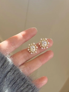 Macro shot of gold-plated flower earrings with oval zircon stones and pearl borders