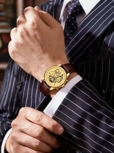 Close-up of men's skeleton watch with gold case and brown leather strap on suit wrist