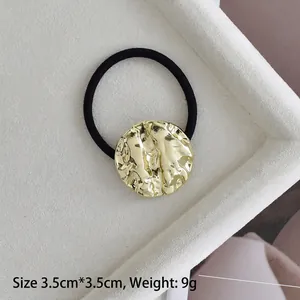 Detail of 3.5cm gold alloy hair tie with hammered texture on a velvet tray