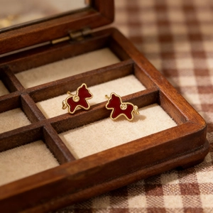 Close-up of red flocked pony earrings with pearls and gold accents in a wood tray