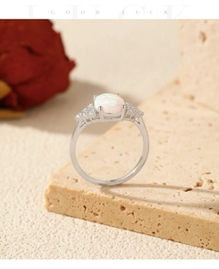 Macro detail of oval white opal ring with small zircon stones on beige stone display