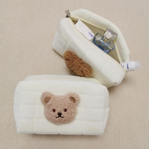 Close-up of quilted cosmetic bag with cute brown plush bear patch and zipper detail