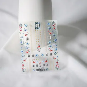 Floral nail art stickers with red and blue flower designs and gold dots on white fabric