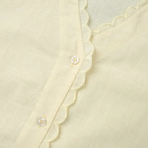 Détail du col en V avec bordure festonnée et boutons sur ce haut beige en lin de coton