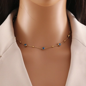 Close-up of golden evil eye necklace with blue charms on model wearing beige blazer