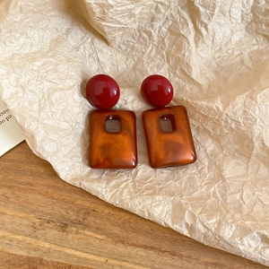 Close-up of vintage geometric acrylic earrings with red studs and amber square pendants