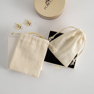 Flat lay of beige cotton jewelry drawstring bags with golden earrings and bracelet