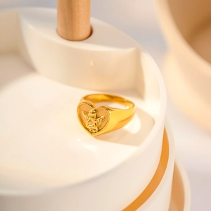 Gold heart-shaped signet ring with angel relief on a white ceramic jewelry dish
