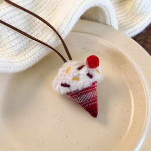 Close-up of handmade ice cream cone pendant with embroidery and soft red pom-pom detail