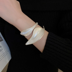 Macro detail of leaf shaped matte silver cuff bracelet worn over black knit clothing