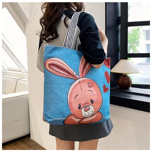 Blue canvas tote bag with pink cartoon rabbit print and striped strap worn by a model