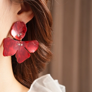 Close-up model wearing large dark red resin flower earrings with marble pattern