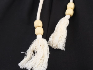 Dettaglio cintura in cotone crema con perline di legno e nappe su pantaloni neri
