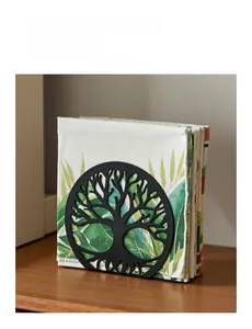 Vertical black metal napkin holder with laser-cut tree of life design on wooden table