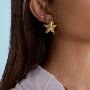 Close-up of a model wearing minimalist golden starfish earrings with a metallic finish