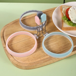 Tre stampi per uova in silicone colorati con manici in metallo su un tagliere di legno