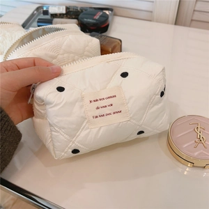 Détail de la trousse de maquillage matelassée blanc crème avec pois noirs et étiquette