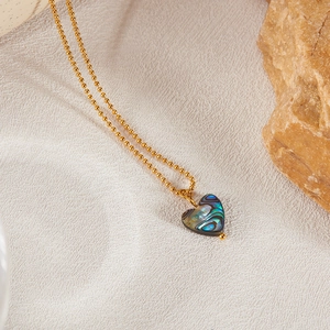 Detail of a heart-shaped abalone shell pendant on a golden bead chain against textured stone