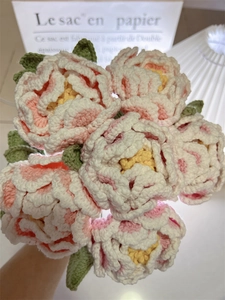 Close-up of handmade crochet peony bouquet with pink petals and green leaves in a vase