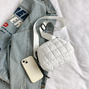 Flat lay of a white quilted crossbody bag with wide strap on a blue denim jacket