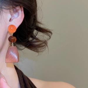 Close-up of geometric earrings with orange beads and brown wood pendants on a model