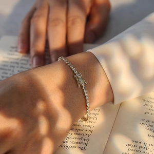 Detail of gold tennis chain bracelet with white cubic zirconia worn on wrist over a book
